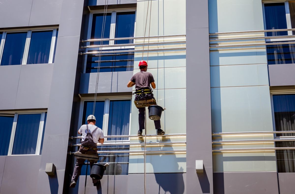 Two industrial climbers are washing, cleaning facade of a modern office building