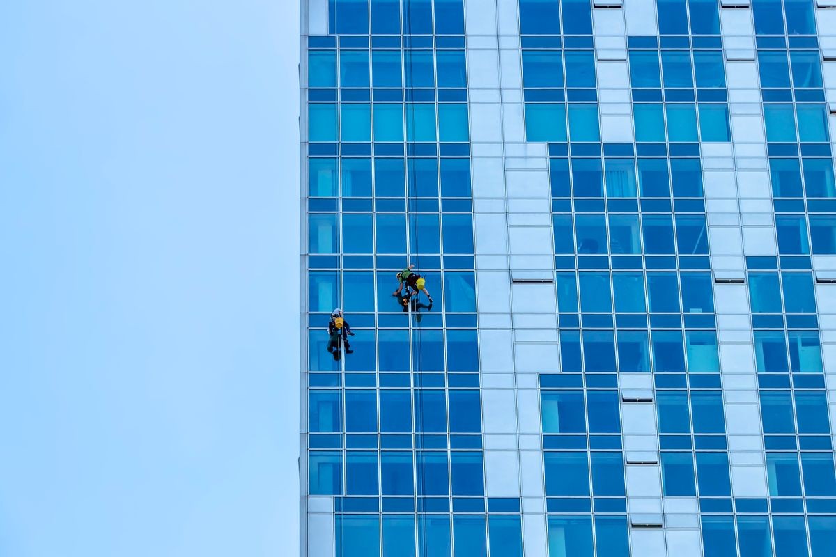 Window washers cleaning the glass facade of a modern building, high risk work